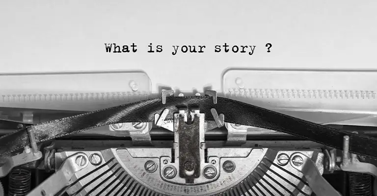 Close-up of a vintage typewriter with a sheet of paper displaying the typed phrase “What is your story?” in black typewriter font. The image is in black and white, emphasizing the nostalgic feel of storytelling through written words.