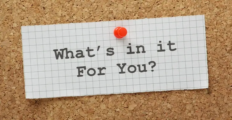 A piece of graph paper pinned to a corkboard with a red thumbtack displays the question “What’s in it For You?” in bold, black type. The image suggests a focus on benefits, value propositions, or personal incentives.