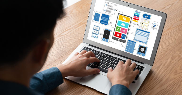 Man working on a laptop displaying a colorful wireframe layout for a mobile app, highlighting the structure and visual design of a digital interface.