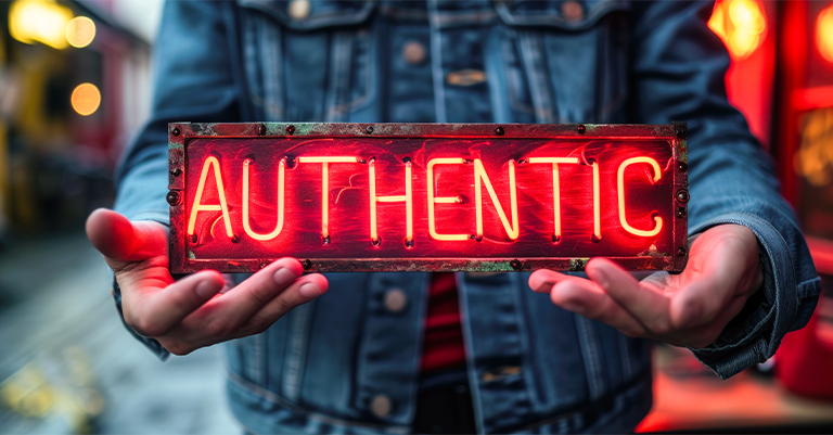 A person in a denim jacket holds a glowing neon sign that reads "AUTHENTIC," symbolizing the importance of originality and realness.