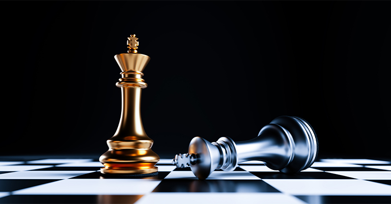 Gold king chess piece standing victorious next to a fallen silver king on a black and white chessboard, symbolizing success and strategy.