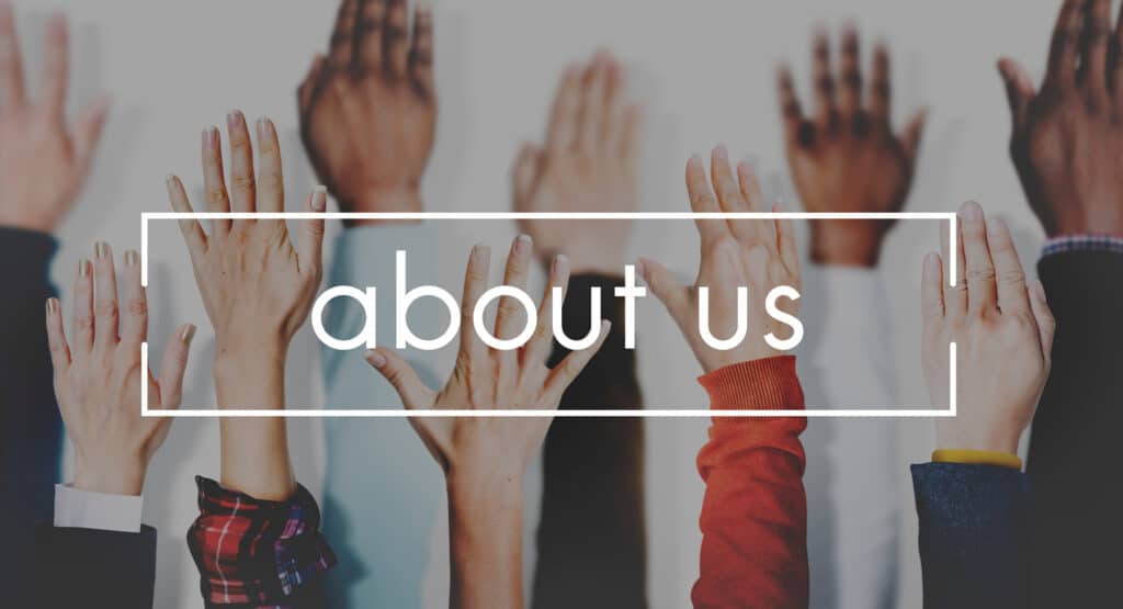 Image of diverse hands raised against a light background, with the words “about us” in bold white font overlaid inside a rectangular frame. The visual emphasizes community, inclusion, and openness, often used to introduce a team or organization.