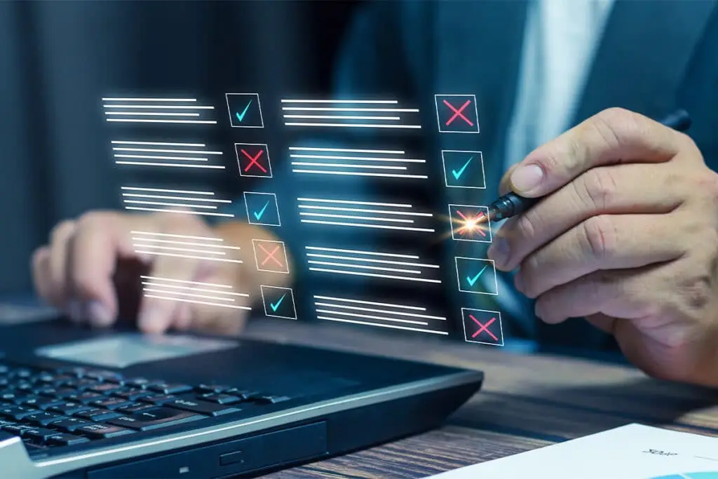 Digital Footprint Audit checklist overlay showing a person reviewing items with check marks and X marks while working on a laptop. A hand holds a pen near the list to suggest evaluating and correcting online information.