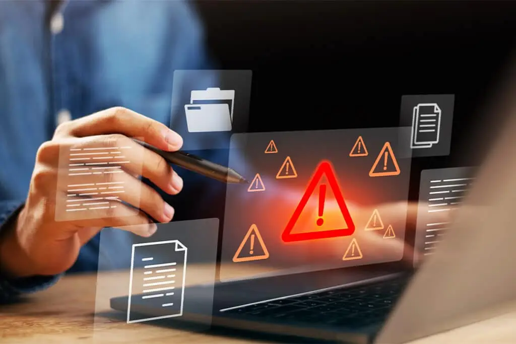 Digital Footprint Audit warning graphic showing a person using a stylus on a laptop with floating document icons and multiple alert symbols including a large red exclamation triangle. The image conveys spotting risky files or problematic online information and flagging issues to address.