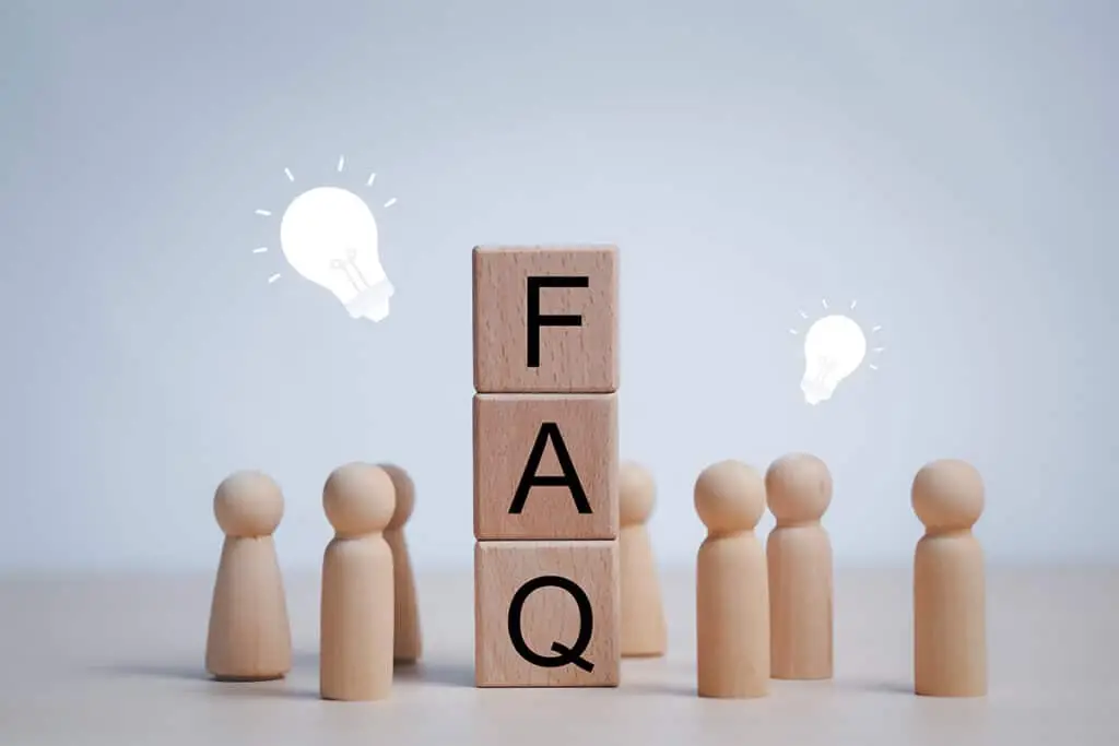 Digital Footprint Audit concept image showing wooden blocks stacked to spell FAQ surrounded by small wooden figures and light bulb icons. The scene suggests common questions and guidance for reviewing and improving an online presence.