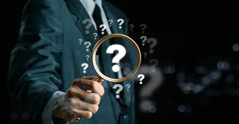 A businessperson holds a magnifying glass over a glowing "?" with more question marks floating around them. The dark background and search motif suggest reflection and self inquiry while working to identify your personal values.