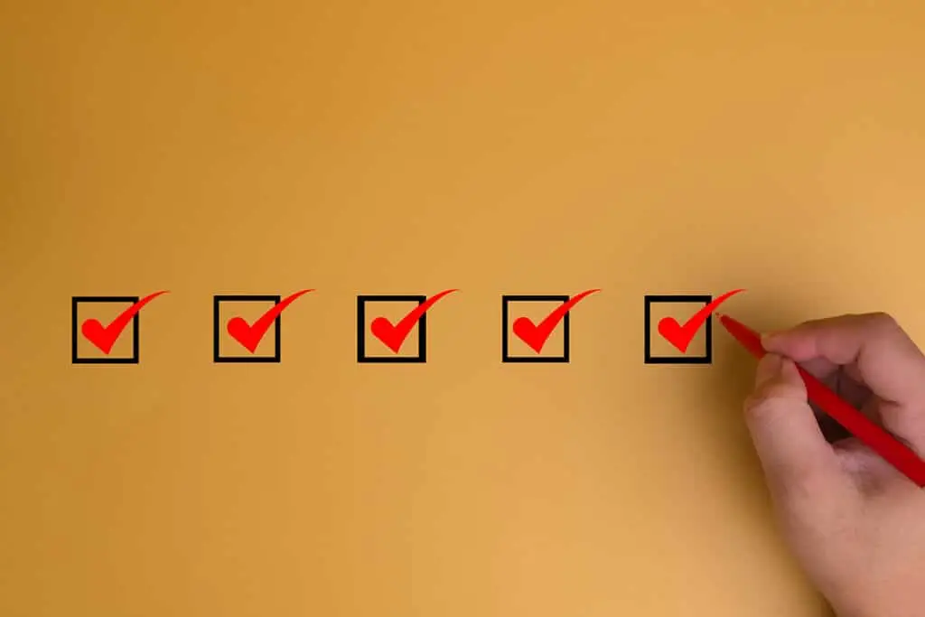 A row of five checkboxes with red check marks appears on a tan background. A hand holding a red pen marks the final checkbox to suggest completing a checklist or confirming tasks are done.