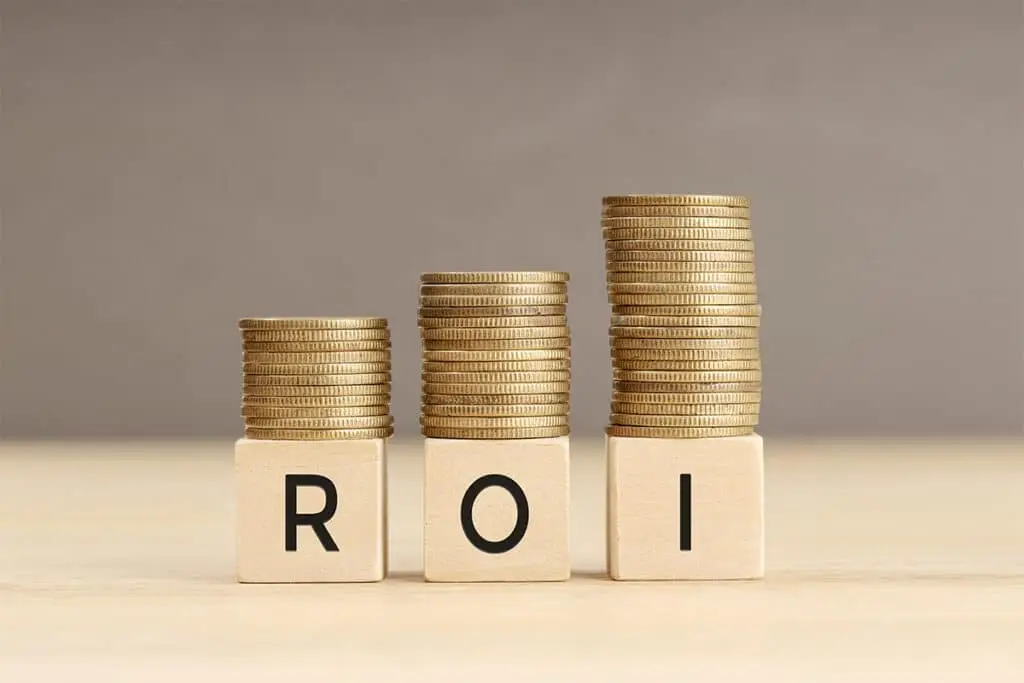 Stacks of coins sit on three wooden blocks labeled ROI with the piles increasing in height from left to right. The image illustrates return on investment with growing money over time.