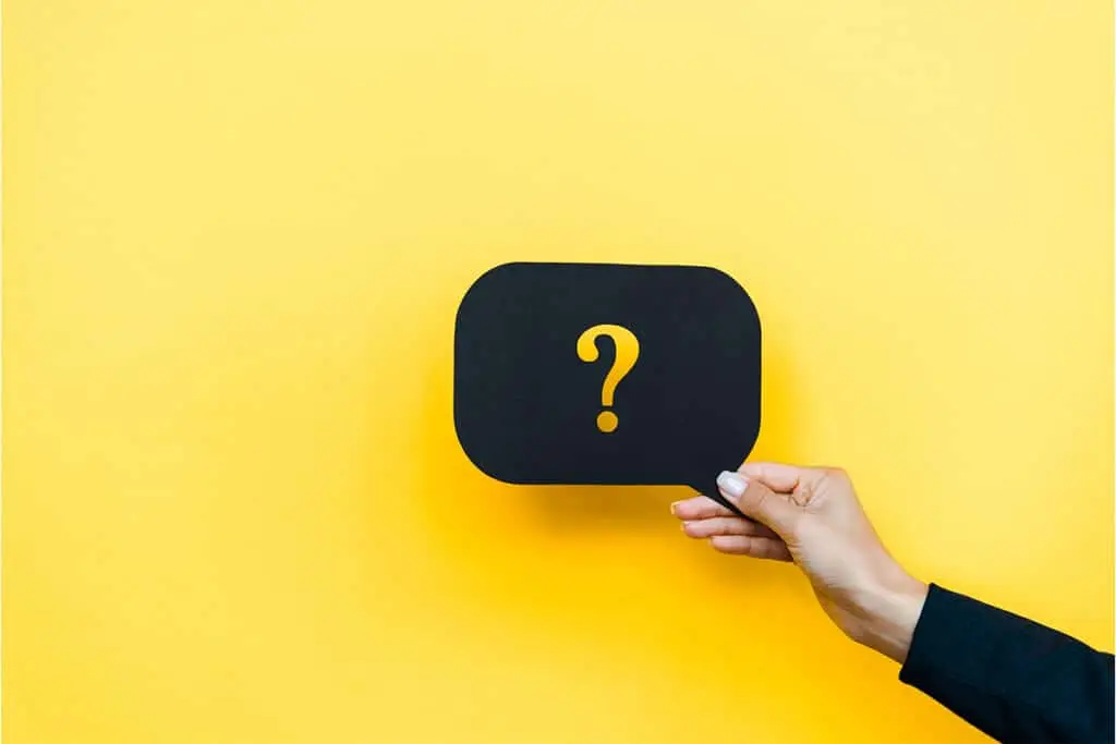 A hand holds a black speech bubble card with a yellow question mark against a bright yellow background. The image suggests an unanswered question or uncertainty that could impact a positive professional online reputation.