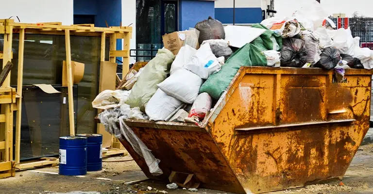An overflowing rusty dumpster is packed with trash bags and discarded materials outside a building. It can represent messy search results or unwanted online content that needs cleanup when you protect your online reputation.