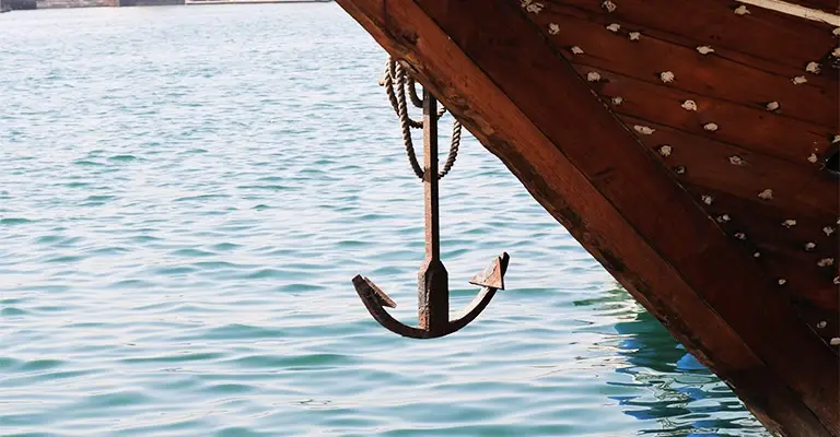 A metal anchor hangs from the bow of a wooden boat above calm blue water. The anchor can suggest strengthening reliable search results that help protect your online reputation.