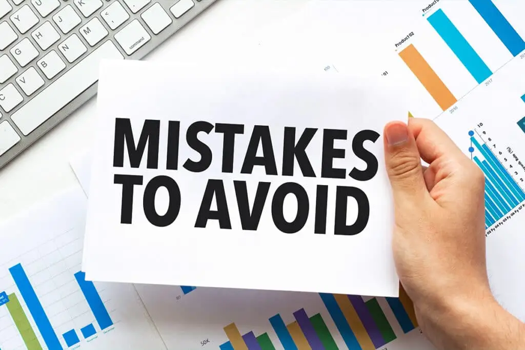 A hand holds a sheet of paper that reads Mistakes to Avoid, placed over charts and a computer keyboard on a desk. The image suggests common pitfalls to watch for as you Build a Personal Brand.
