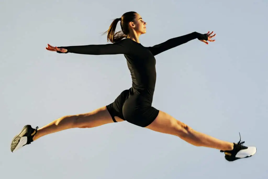 A person in black athletic wear leaps through the air in a wide split jump against a clear sky background. The image conveys confidence and momentum as you Build a Personal Brand by showing energy and standout presence.