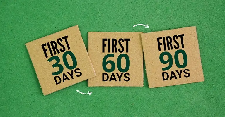 Three cardboard signs on a green background read "FIRST 30 DAYS." "FIRST 60 DAYS." and "FIRST 90 DAYS." Small arrows connect the stages to show a structured timeline for building your brand on LinkedIn.