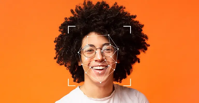 A smiling young person with curly hair and glasses faces the camera against a bright orange background. A white facial recognition grid and corner frame overlay their face. This connects the portrait to personal branding for students and how digital identity can be shaped online.