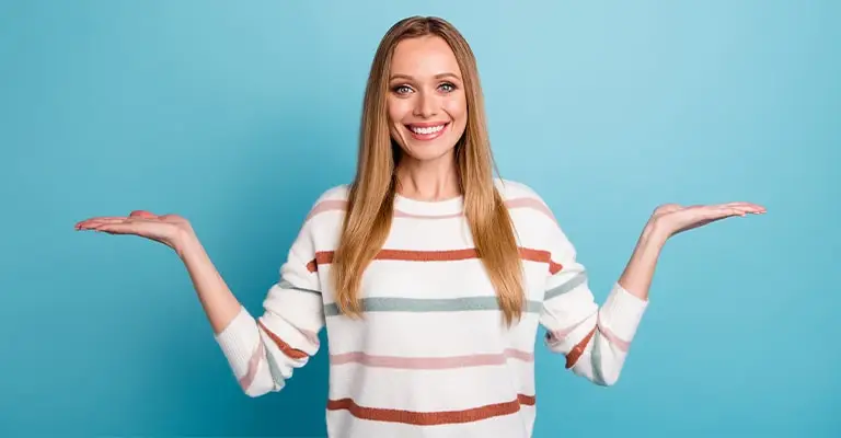 A smiling young woman in a striped sweater stands against a teal background with both palms raised as if presenting two options. The open pose fits a personal branding for students article about choosing how to show your strengths and personality.