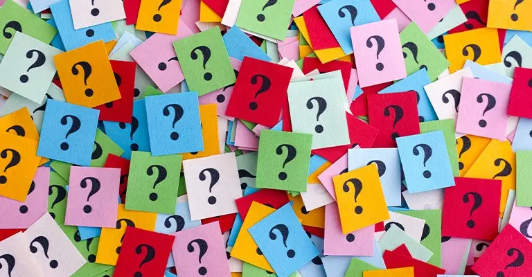 A scattered pile of colorful paper cards each printed with a large black question mark. The unanswered questions represent the challenges and decisions involved when working to optimize your social media.